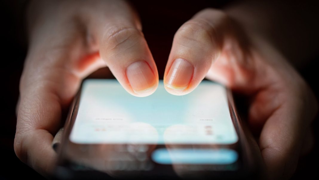 close up of two woman's thumbs touching on a smartphone screen in the dark.